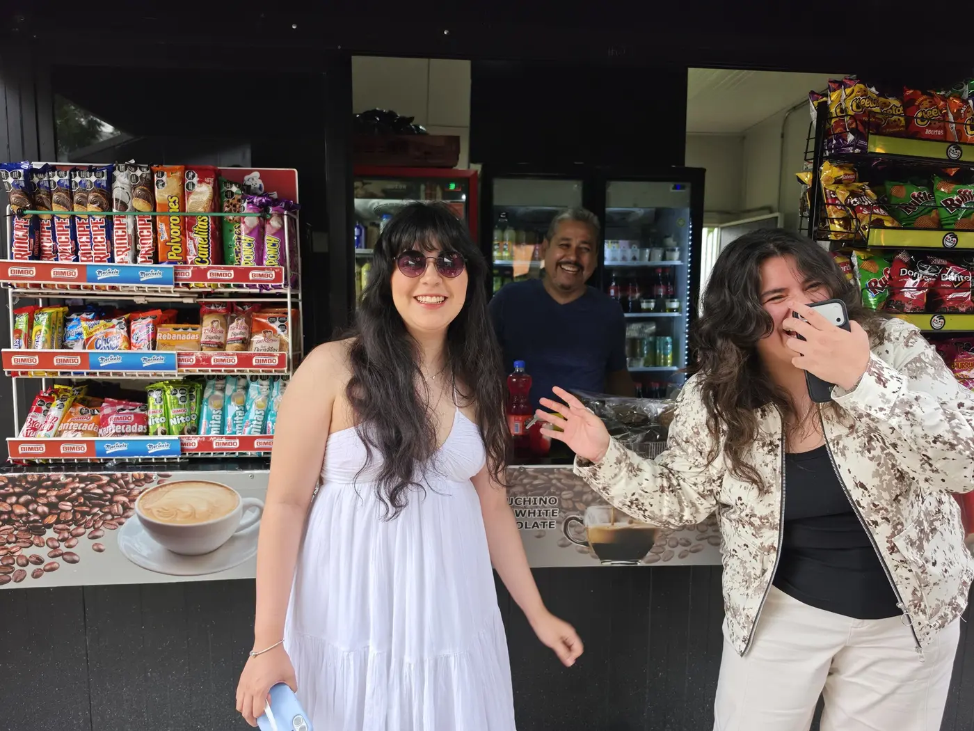 Dos clientas riendo frente al mostrador, Don Poncho sonriendo al fondo